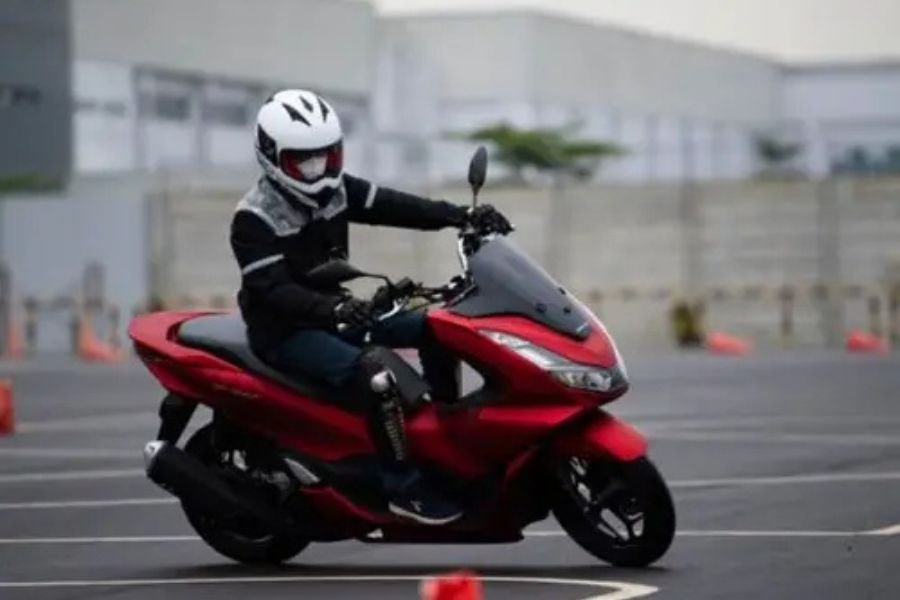 pengendara motor Honda mengenakan helm berwarna cerah yang mudah terlihat di jalan, meningkatkan visibilitas dan keselamatan berkendara terutama saat berada di dekat kendaraan besar seperti truk dan bus.